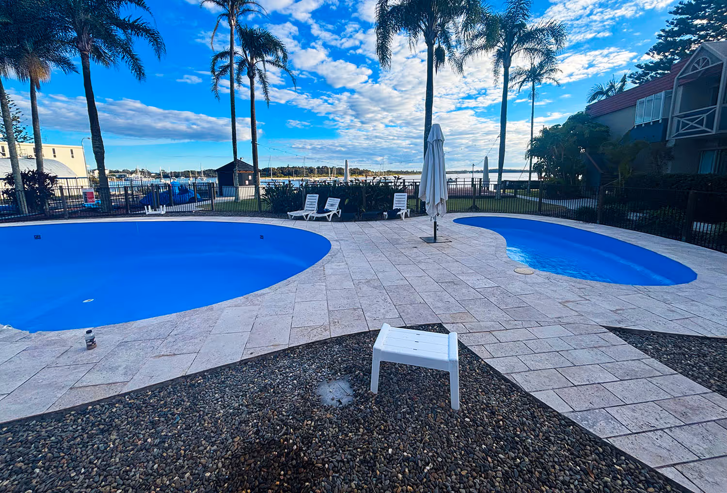 Blue resurfaced pool interiors beside a palm-lined waterfront